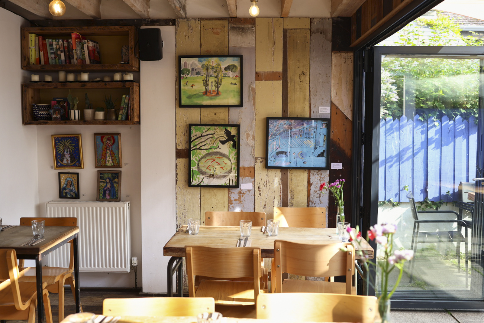 Dining room with wooden tables, artwork on the walls and doors open to the garden at Soulshine, Bridport